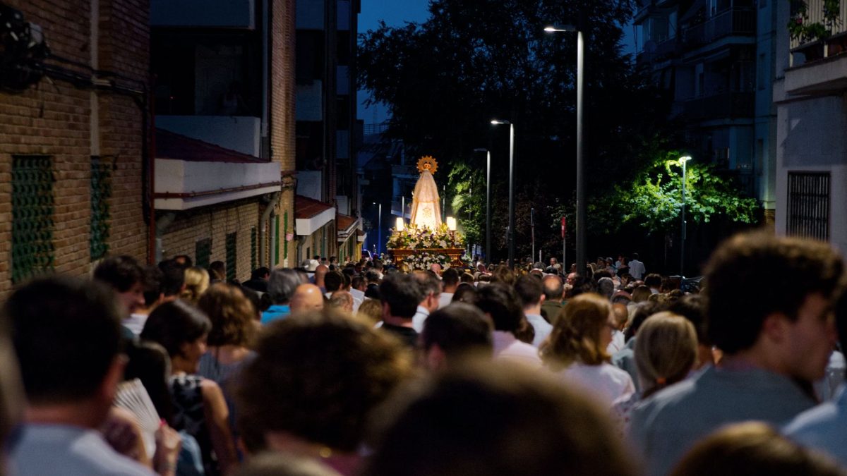 Procissão religiosa reúne pessoas em uma rua movimentada durante a noite.