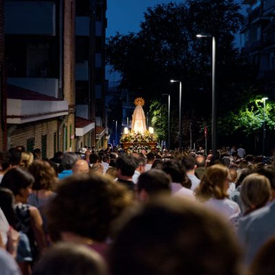 Procissão religiosa reúne pessoas em uma rua movimentada durante a noite.