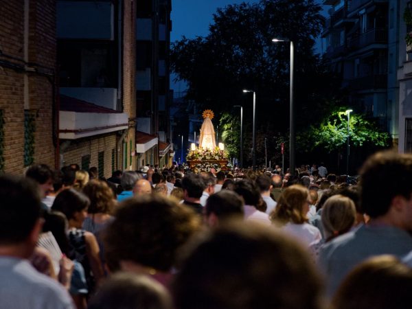 Procissão religiosa reúne pessoas em uma rua movimentada durante a noite.