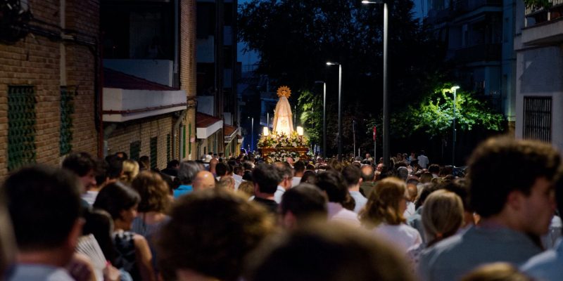 Procissão religiosa reúne pessoas em uma rua movimentada durante a noite.