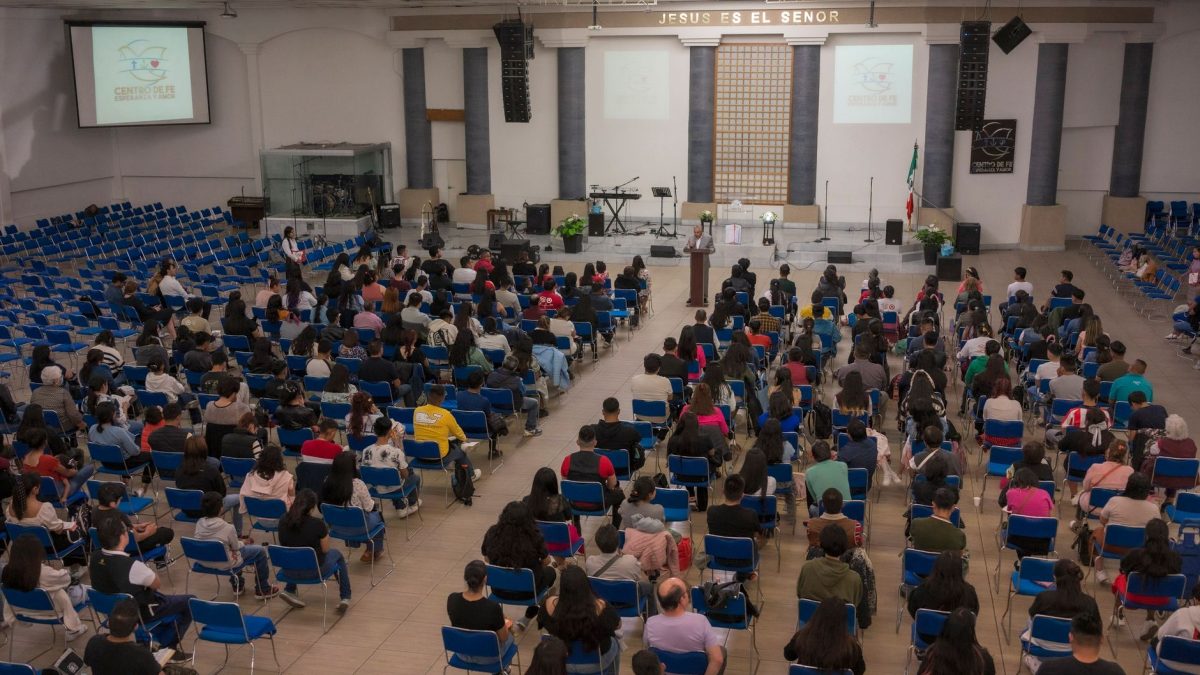 Público numeroso sentado em um auditório de igreja durante um seminário ou conferência.