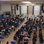 Público numeroso sentado em um auditório de igreja durante um seminário ou conferência.