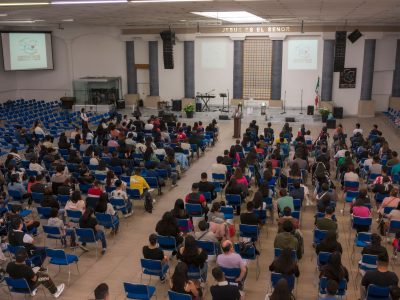 Público numeroso sentado em um auditório de igreja durante um seminário ou conferência.