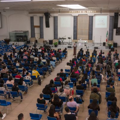 Público numeroso sentado em um auditório de igreja durante um seminário ou conferência.