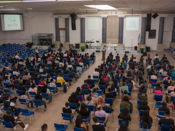 Público numeroso sentado em um auditório de igreja durante um seminário ou conferência.