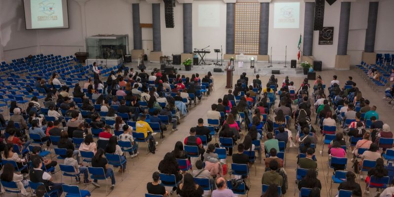 Público numeroso sentado em um auditório de igreja durante um seminário ou conferência.