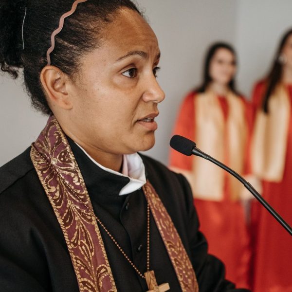 Pastora fala em uma igreja diante de um coral, durante uma atividade religiosa.