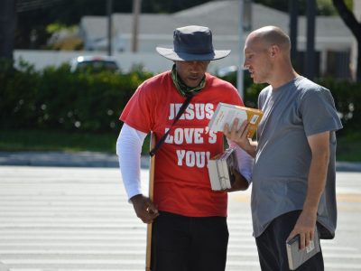 Dois homens conversam em uma rua, segurando livros durante uma abordagem religiosa