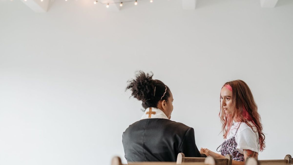 Pastora conversa com outra mulher em um ambiente tranquilo de uma igreja.
