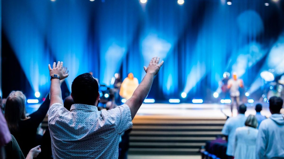 Grupo de pessoas participa de um culto em um auditório moderno.
